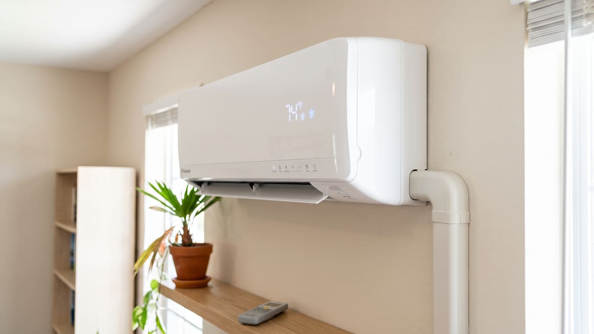 A white wall-mounted mini-split head indoors, its display reading 74 degrees. The line-set cover runs down the wall beside it.