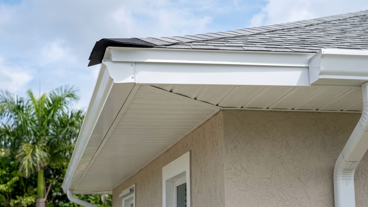 White vented soffit panels and fascia under the eave of a beige stucco Florida home. The perforations are visible along the run.