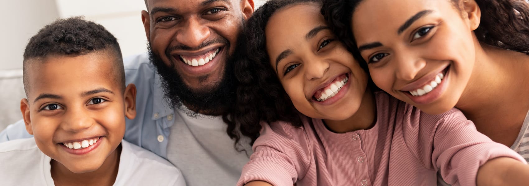 A father, mother, son, and daughter smiling closely together indoors in a selfie-style photo