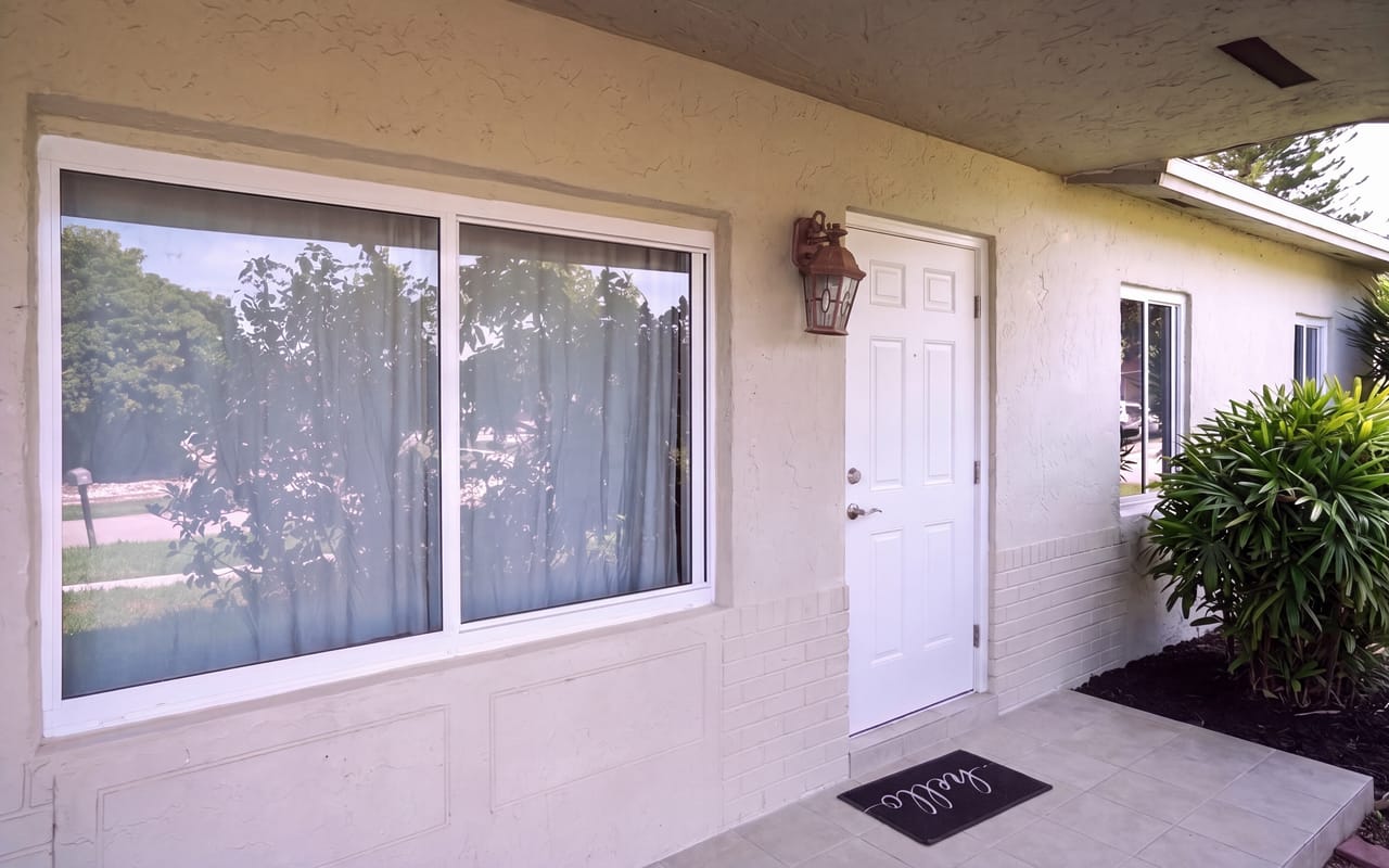 Front entry of a single-story Florida home after installation: a white-framed two-panel impact sliding window and a white impact entry door under a covered porch