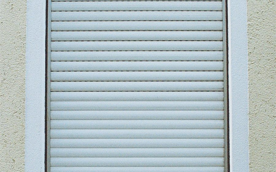 Closed white roller storm shutter over a window on a stucco home