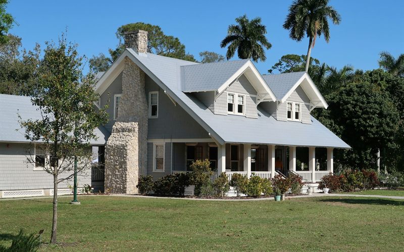 Florida bungalow with a metal roof, a stone chimney, and palm trees